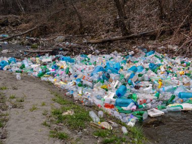 CLOSE UP: Enormous pile of various plastic bottles floating trapped in a branch. Sad view of polluted river with thrown plastic garbage. Numerous accumulated plastic bottles floating on river surface