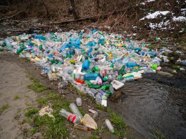 TIRANA, ALBANIA, MARCH 2022: Accumulated plastic packaging and bottles floating stuck in the river. Sad view of littering and environmental damage. Urgent need to establish efficient waste management.