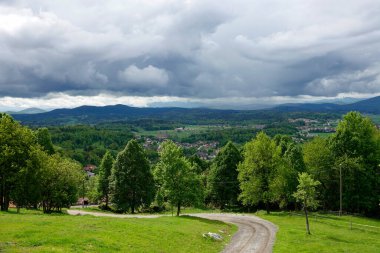 Beautiful view winding macadam path and hilly countryside with rolling gray storm clouds. Picturesque sight of cloudy rural landscape with many hills, valleys and small villages before summer rain.