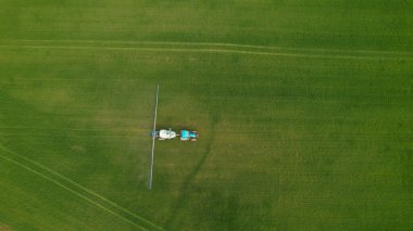 Modern tarım ekipmanlarıyla dolu mavi traktör ekin tarlasını gübreliyor. Çalışan çiftçi, modern tarım ekipmanlarıyla ekili tarlaları koruyor. Tarlayı sulayan bir traktörün görüntüsü.