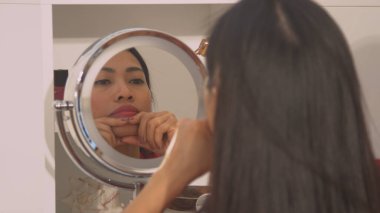 Cosmetic mirror reflection of young lady self massaging her pretty face. Beautiful woman during relaxing face treatment for facial muscle relief. Female person at facial beauty treatment.