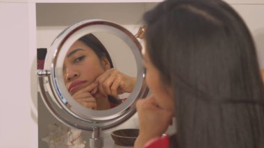 Reflection of pretty young woman performing anti-aging facial massage. Beautiful lady during relaxing face rejuvenating treatment. Female person taking care of her appearance at home bathroom