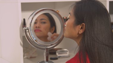 Side view of pretty woman using jade scraper for facial massage. Beautiful young Asian woman with cosmetic mirror performing anti-aging massage treatment with gua sha scraper.