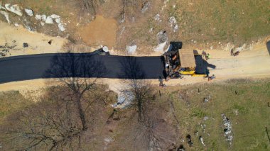 İnşaatçılar asfalt silindiri kullanarak yeni asfalt döşenmiş yolları düzleştiriyorlar. İnşaat işçileri pürüzsüz ve yeni asfaltlanmış garaj yolunu güzel sabah ışığında makinelerle düzleştiriyorlar..