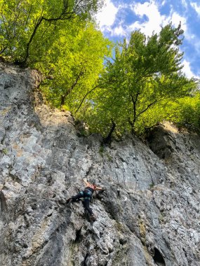 Fit sporty woman lead climbing in the middle of steep rocky wall. Woman ascending up the steep climbing route. Intense physical and mental activity in surroundings of beautiful nature.