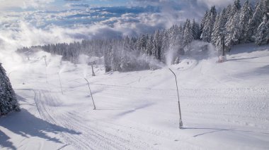 Snowmakers spraying artificial snow at ski resort with gorgeous view. Snow preparation for consolidating snow base at ski slopes and a long winter season. Winter wonderland in the mountains.