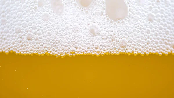 MACRO, DOF: Tiny bubbles form the foam on top of a glass full of pale ale beer. Close up shot of a crisp pint of golden lager with perfect white foam. Detailed macro of a foamy jug of refreshing beer.