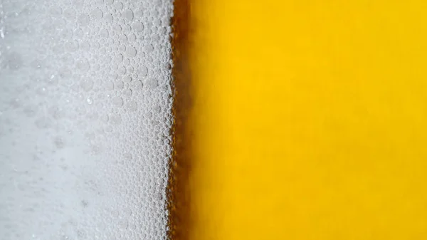 VERTICAL, MACRO, DOF: Detailed macro of a foamy jug of refreshing alcoholic beer. Tiny bubbles form the foam on top of a glass full of an ale. Close up shot of a pint of lager with perfect white foam.