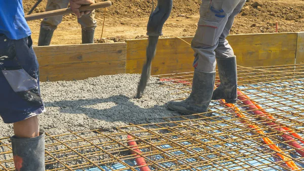 CLOSE UP: Builders pour the wet cement mixture over a layer of metal mesh. Contractors pour rough wet concrete over a reinforced steel net while creating the foundation of a modern housing projects.