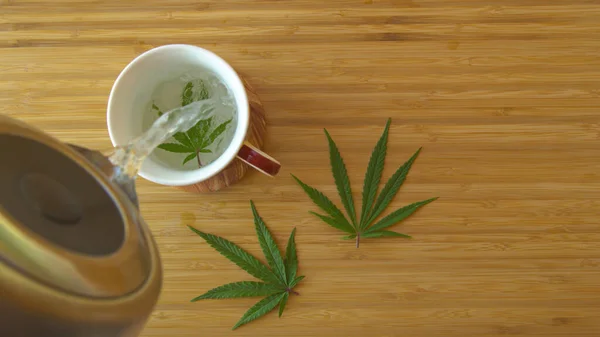 Boiling Water Gets Poured Marijuana Leaf White Teacup Sitting Wooden — Stockfoto