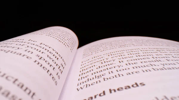 CLOSE UP, BOKEH: Detailed view of page content in an open book on black background. Words and paragraphs of the open handbook in shallow focus. book sheet details with written content forming pattern.