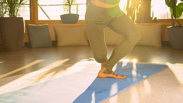 Fit young woman doing cross lunge squats in beautiful golden light. Sporty lady in sportswear during bodyweight training doing exercises for leg and lower back muscles and body stability.
