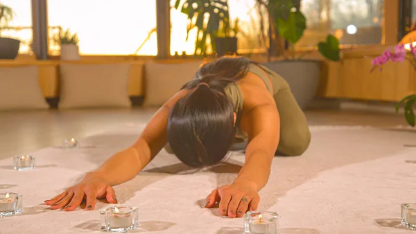 Pretty Asian woman in restful yoga pose in relaxing home atmosphere. Young Asian female person doing yoga practice at home. Healthy indoor leisure activity for relaxation and flexibility.