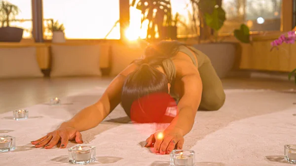Pretty Asian woman at restful yoga pose in relaxing home atmosphere. Young Asian female person doing yoga practice at home. Healthy indoor leisure activity for relaxation and flexibility.