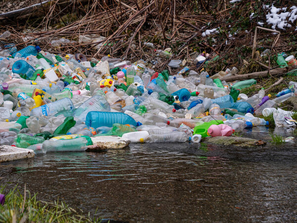 CLOSE UP: Accumulated pile of various plastic bottles caught at the river edge. Worrying view of the polluted river with thrown plastic rubbish. Accumulated plastic bottles floating on river surface.