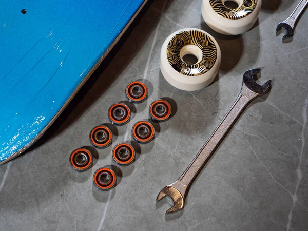 LA, UNITED STATES, APRIL 2022: TOP DOWN: Close up view of lined up skateboard bearings and wheels with wrench. Ordered sequence of individual skateboard parts and tool on countertop ready for assembly