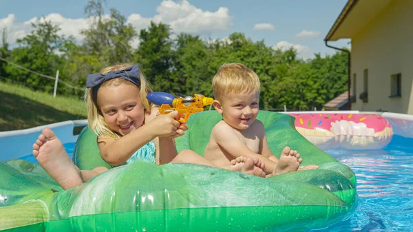 亲密接触 快乐的兄妹在游泳池里玩水枪 炎炎夏日的水上运动3 孩子们在自家后院的游泳池里玩耍时 玩得很开心 — 图库照片
