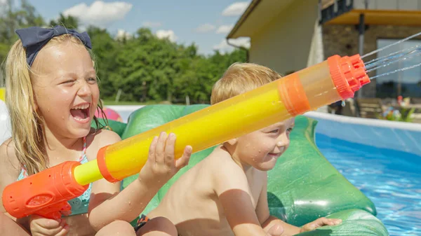 快乐的兄妹在游泳池里用水枪喷射 在后院里的游泳池派对上 快乐的孩子们欢笑着 享受着水上运动 在夏天泼洒食水作茶点 — 图库照片