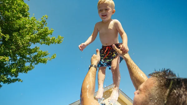 低角度概述 父亲在游泳池里玩耍的时候把他的小儿子抛向空中 夏天的一天 在自家后院的游泳池里玩乐 快乐的孩子在空中享受着 — 图库照片
