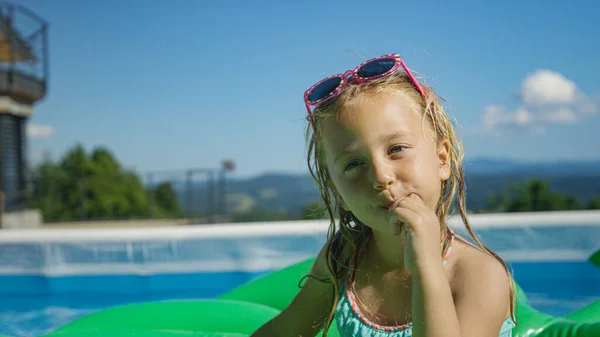 CLOSE UP: Adorable little girl finishing her ice cream in garden swimming pool. Cute girl enjoying chocolate ice cream bar in backyard garden pool. Complete refreshment on a hot sunny summer day.