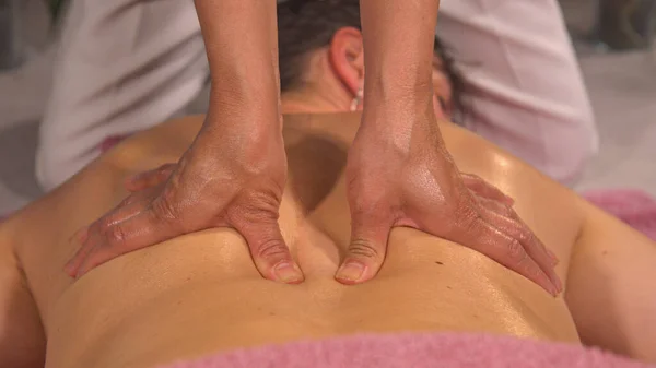 Professional massage therapist is treating a young female patient. Relaxation, beauty, body and face treatment concept. Detailed view of female hands performing back muscle relief massage.
