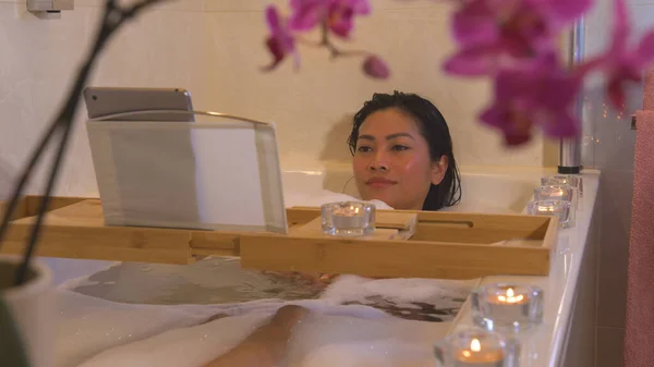 リラックスした若い女性が泡風呂に横たわって オンライン映画を見ています 美しいフィリピンの女性は忙しい一日の後にバスタブでリラックスし デジタルタブレットで彼女のお気に入りのシリーズを見て — ストック写真
