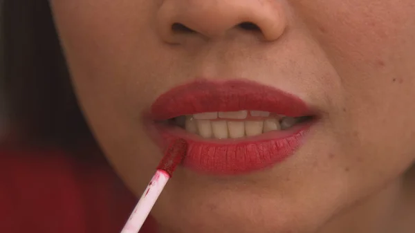 Detailed shot of young female lips after applying shiny red lip gloss. Pretty young lady using colourful and vibrant cosmetic product for lips. Female person perfecting look using cosmetics.