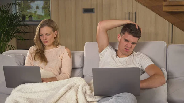 自宅のリビングルームでリモートワークのためのラップトップを使用してカップル 若い男と女性は毛布で覆われたソファに座って 孤独の間に仕事の責任を果たすためにラップトップを使用しています — ストック写真
