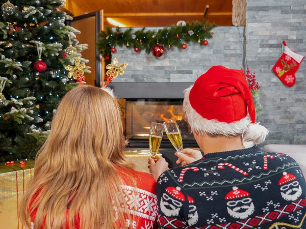 暖炉を見てシャンパンで乾杯する若いロマンチックなカップル 美しく装飾された家のリビングルームで暖炉の前でクリスマスイブを祝う陽気な男と女 — ストック写真
