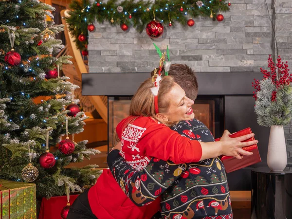 感謝の女性はプレゼントで彼女を幸せにした彼女の夫を包含する 陽気なカップルは 美しく装飾された家のリビングルームで暖炉でクリスマスの休日を楽しんで祝います — ストック写真