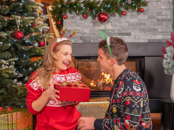 彼女の夫は贈り物で彼女を驚かせたとき 陽気な女性は喜びます 素敵な若いカップルは クリスマスを祝い 美しい装飾された家でお祝いの夜にプレゼントを包んだ交換 — ストック写真
