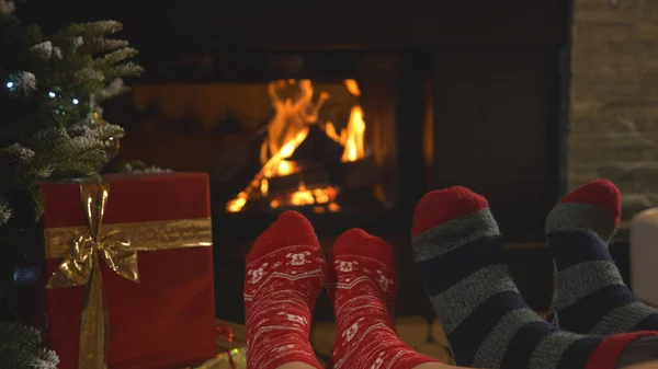 暖炉のそばで休み クリスマスソックスで足を暖めます 男性と女性はクリスマスの夜に美しく装飾されたリビングルームの快適さで楽しんでリラックスしています — ストック写真