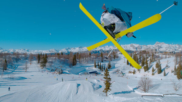 Stunning view of freestyle skier doing grab trick while jumping kicker. Young extreme athlete flying high above snow park and ski area. Adrenaline activity on sunny winter day in ski area.