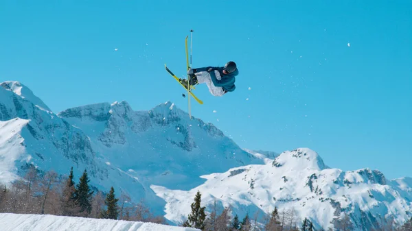 雪に覆われた山々の上を飛ぶ男性のフリースタイルのスキーヤー スキー場のスノーパークで大きなエアキッカーをジャンプする若い極端な選手 スキー場での晴れた冬の日のアドレナリン活動 — ストック写真
