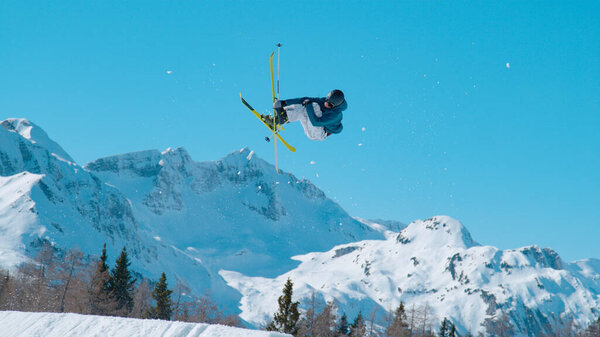 Male freestyle skier flying above snow-covered mountaintops. Young extreme athlete jumping big air kicker at snow park in ski area. Adrenaline activity on sunny winter day in ski area.