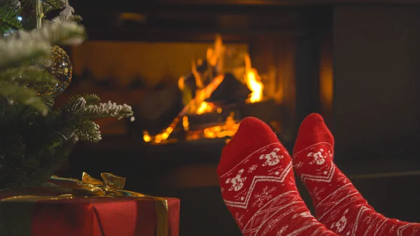 暖炉のそばのクリスマス柄の赤い靴下の女性の足 クリスマスの夜 暖かくてお祝いの家のリビングルームの快適な雰囲気の中で楽しみ リラックスした女性の人 — ストック写真