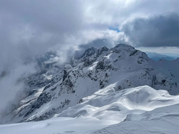 Stunning view of rolling clouds over picturesque mountain peaks after snowstorm. Breath-taking location for mountain adventures in pristine and untouched alpine terrains of snow-covered Albanian Alps.