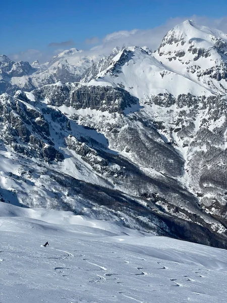 Beautiful snowy mountain scenic with a freeride skier riding fresh powder snow. Unrecognizable skier enjoying riding powder snow in the embrace of picturesque and freshly snow-covered mountains.