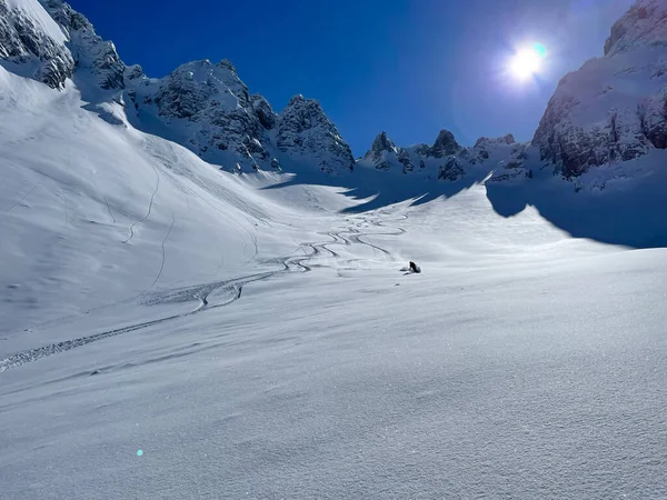Snowy mountain slope with fresh tracks and skier enjoying on fresh powder. Unrecognizable freeride skier enjoying skiing on fresh snow in the embrace of pristine and snow-covered Albanian mountains.