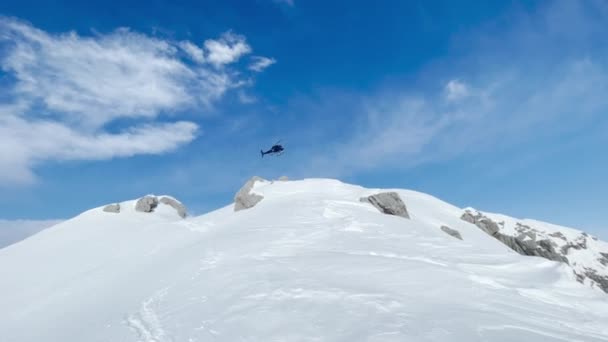 低い角度ビュー ヘリコプターは雪の山を離陸し 谷に向かって飛ぶ 絵のように手付かずの美しいアルバニアの野生の山々での冒険的なフリーライドヘリスキングのための飛行輸送 — ストック動画