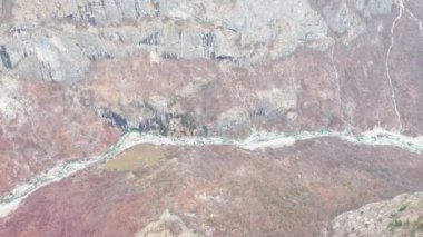 AERIAL: View through helicopter window while flying over wild river and valley. Stunning scenery with green river in narrow canyon, steep slopes and high snow-covered mountains in wild Albanian Alps.
