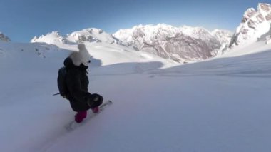 Young female snowboard rider enjoys riding down freshly snow-covered mountain. Picturesque and joyful freeride on fresh powder snow. Lady spraying snow while making snowboard turns on snowy slope.
