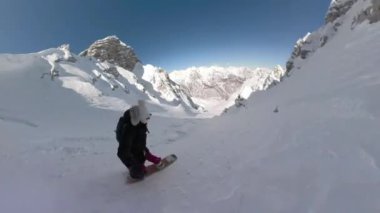 Young lady on a joyful freeride spraying fresh snow while making snowboard turns on snowy mountain slope. Female snowboarder enjoying riding powder snow in the embrace of freshly snowed mountains.
