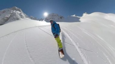 Young male snowboarder enjoys riding down freshly snow-covered mountain slope. Picturesque and joyful freeride on fresh powder snow. Man spraying snow while making snowboard turns on snowy mountaintop