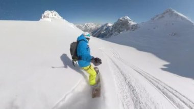 Young guy on a joyful freeride spraying fresh snow while making snowboard turns on snowy mountain slope. Male snowboarder enjoying riding powder snow in the embrace of freshly snow-covered mountains.