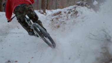 SLOW MOTION: Rear view of mountain biker spraying snow at riding corner on trail. Fun bike ride in the woods after fresh snowfall. Spice of adrenaline during mountain biking in winter conditions.