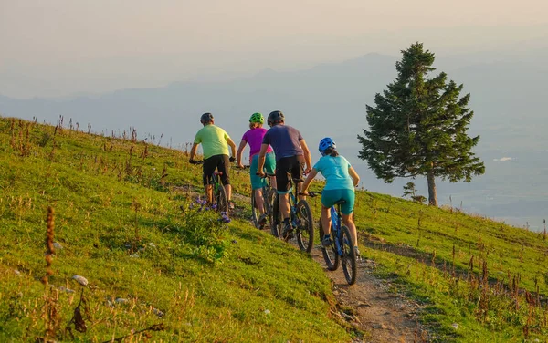 Group of mountain bikers pedalling their electric bikes up a narrow dirt road. Unrecognizable young friends on an active holiday enjoying an cross country bicycle ride in the sunny Slovenian mountains