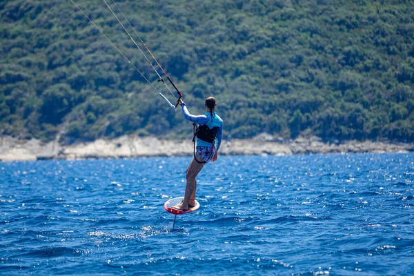 CLOSE UP, DOF: Relaxed young woman foilsurfs towards the Mediterranean shoreline on a sunny summer day. Unrecognizable female tourist surfs on a foil board towards the untouched Peljesac peninsula.