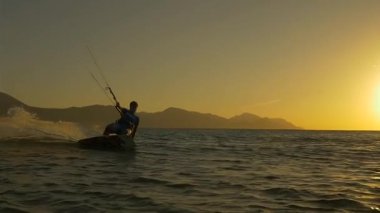 SLOW MOTION: Kiterboarder riding at golden sunset