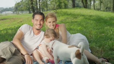 Mutlu genç anne ve baba gülüyor, küçük kız ve sevimli köpekle oynuyor.